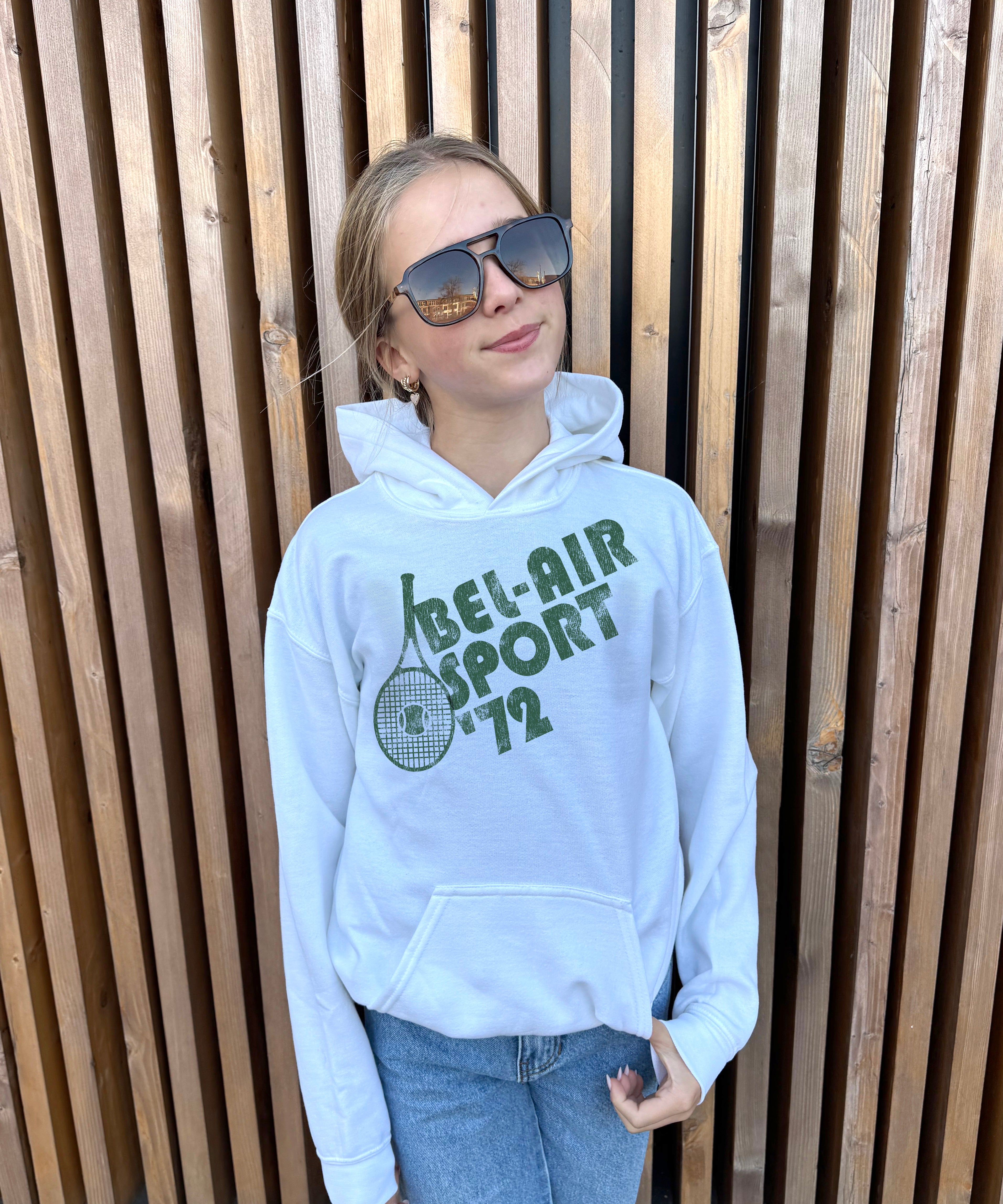 Girl in white hoodie that says "Bel-Air Sport 72" in green text