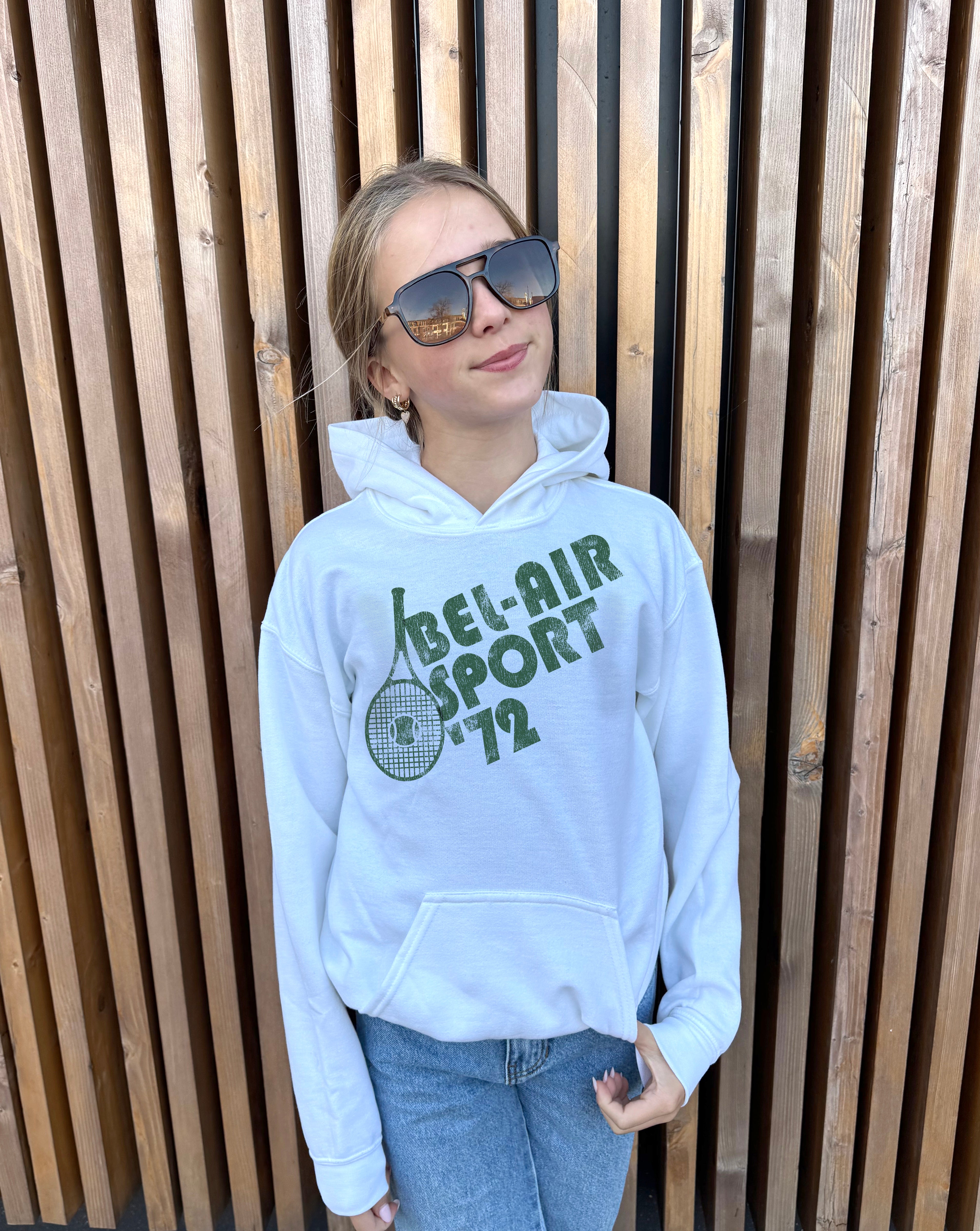 Girl in white hoodie that says "Bel-Air Sport 72" in green text