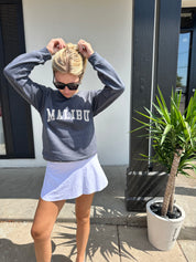 Woman in grey pullover that has white text that says "Malibu"