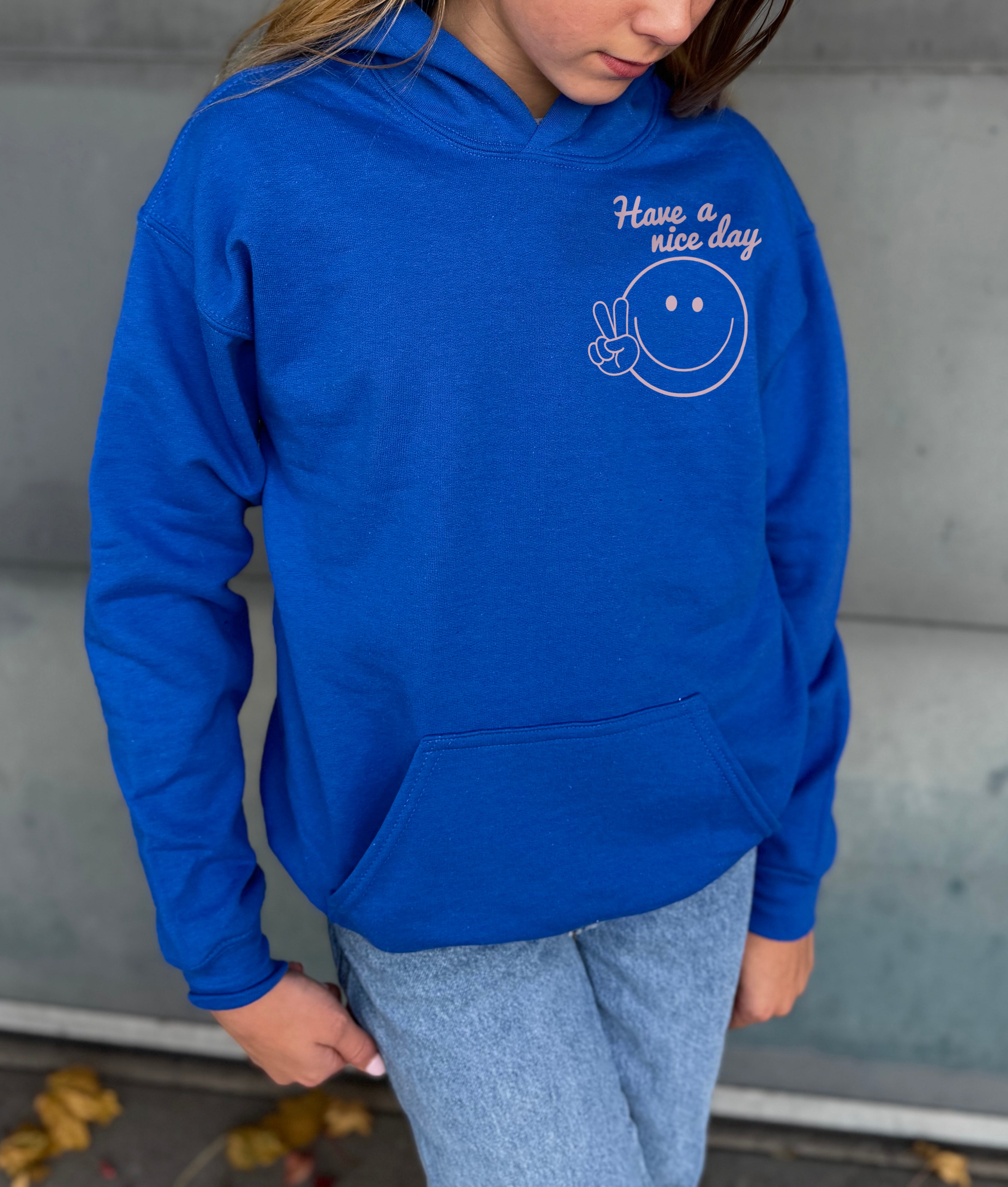 Girl in blue hoodie that says "have a nice day" in pink text with Smiley face
