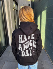 Girl in black hoodie that says "have a nice day" in white text with Smiley face from behind