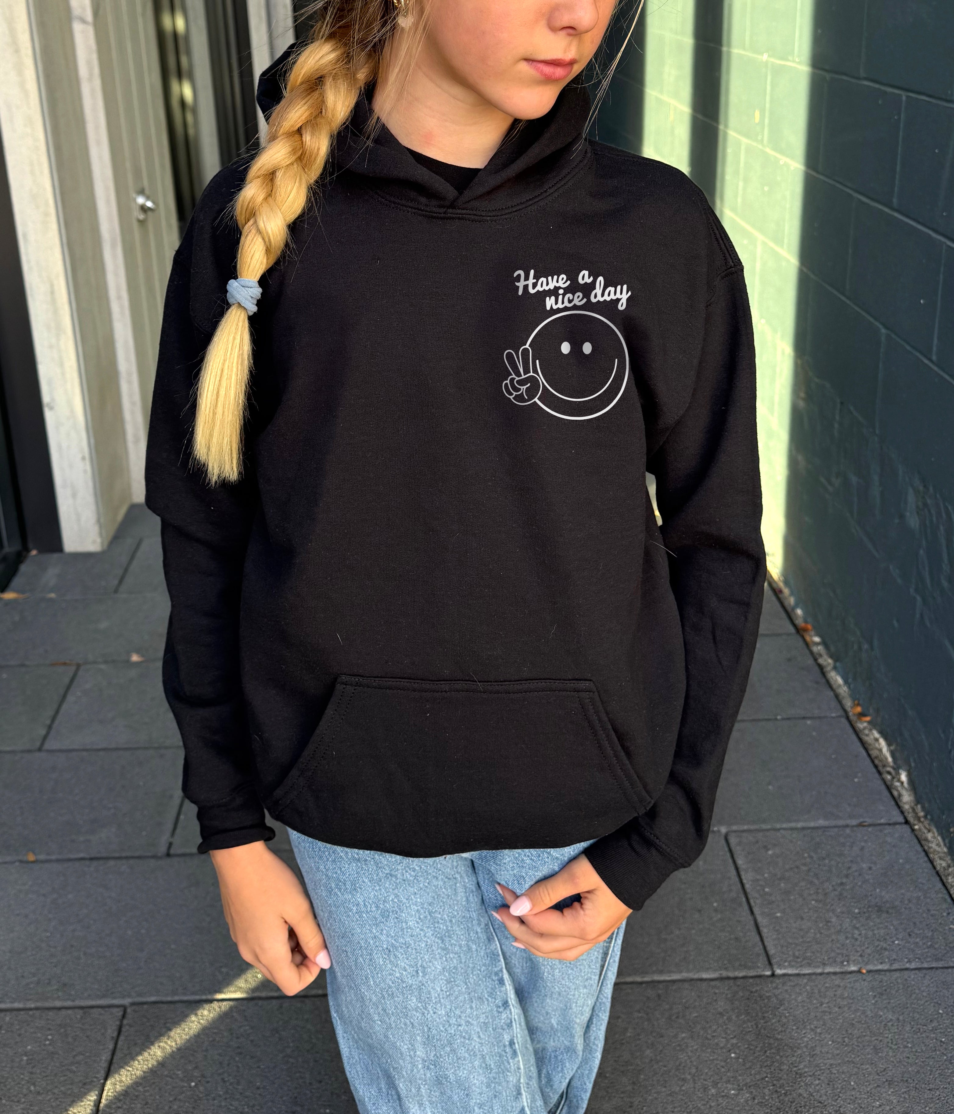 Girl in black hoodie that says "have a nice day" in white text with Smiley face