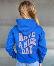 Girl in blue hoodie that says "have a nice day" in light pink text with Smiley face from behind