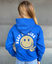 Blue hoodie from the back that says "keep Smiling"  with a yellow smiley with a peace sign