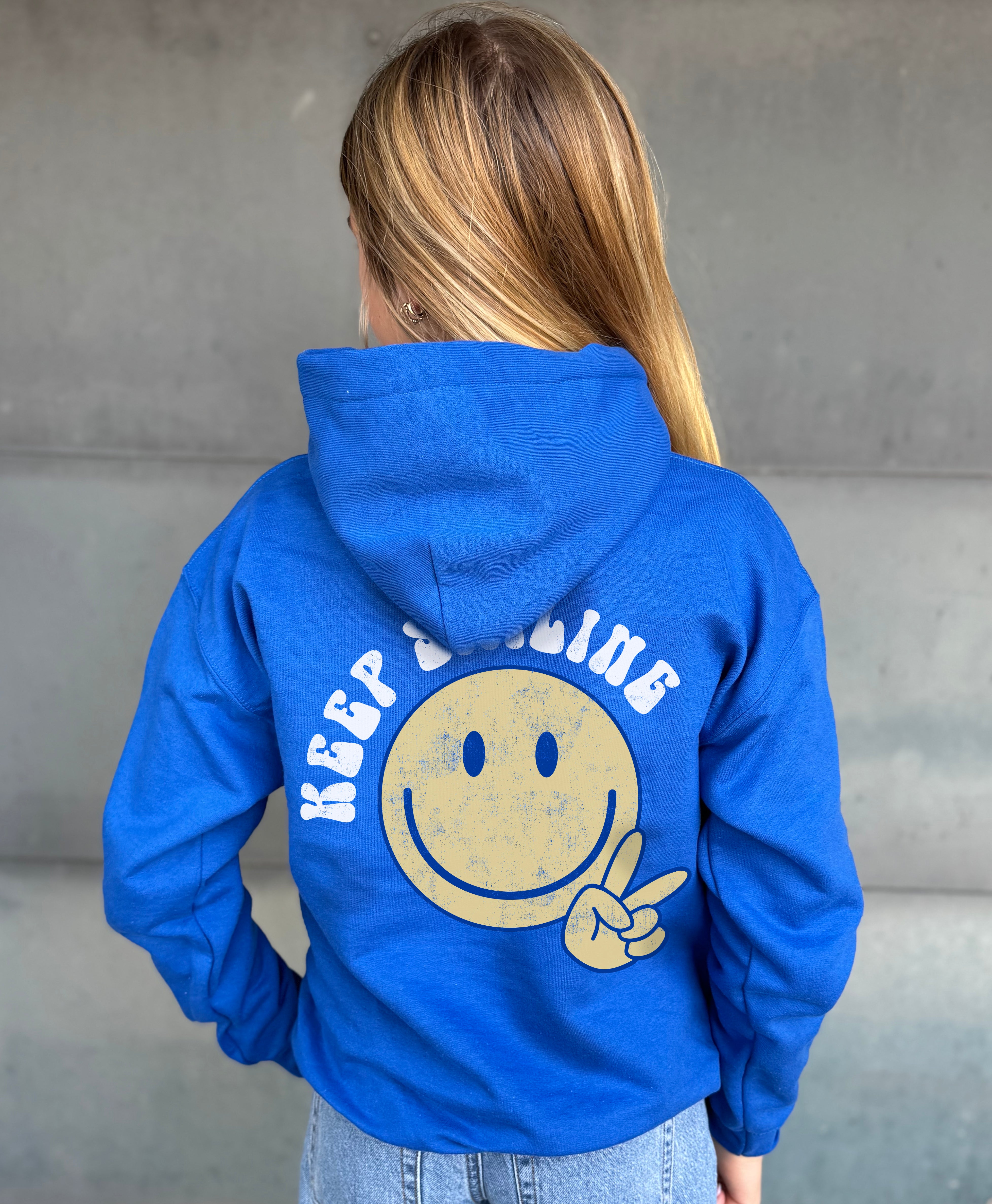 Blue hoodie from the back that says "keep Smiling"  with a yellow smiley with a peace sign