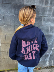 Girl in dark blue hoodie that says "have a nice day" in light pink text with Smiley face from behind