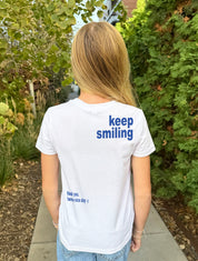Girl in white tee shirt with bluelettering that say "Keep Smiling" from behind