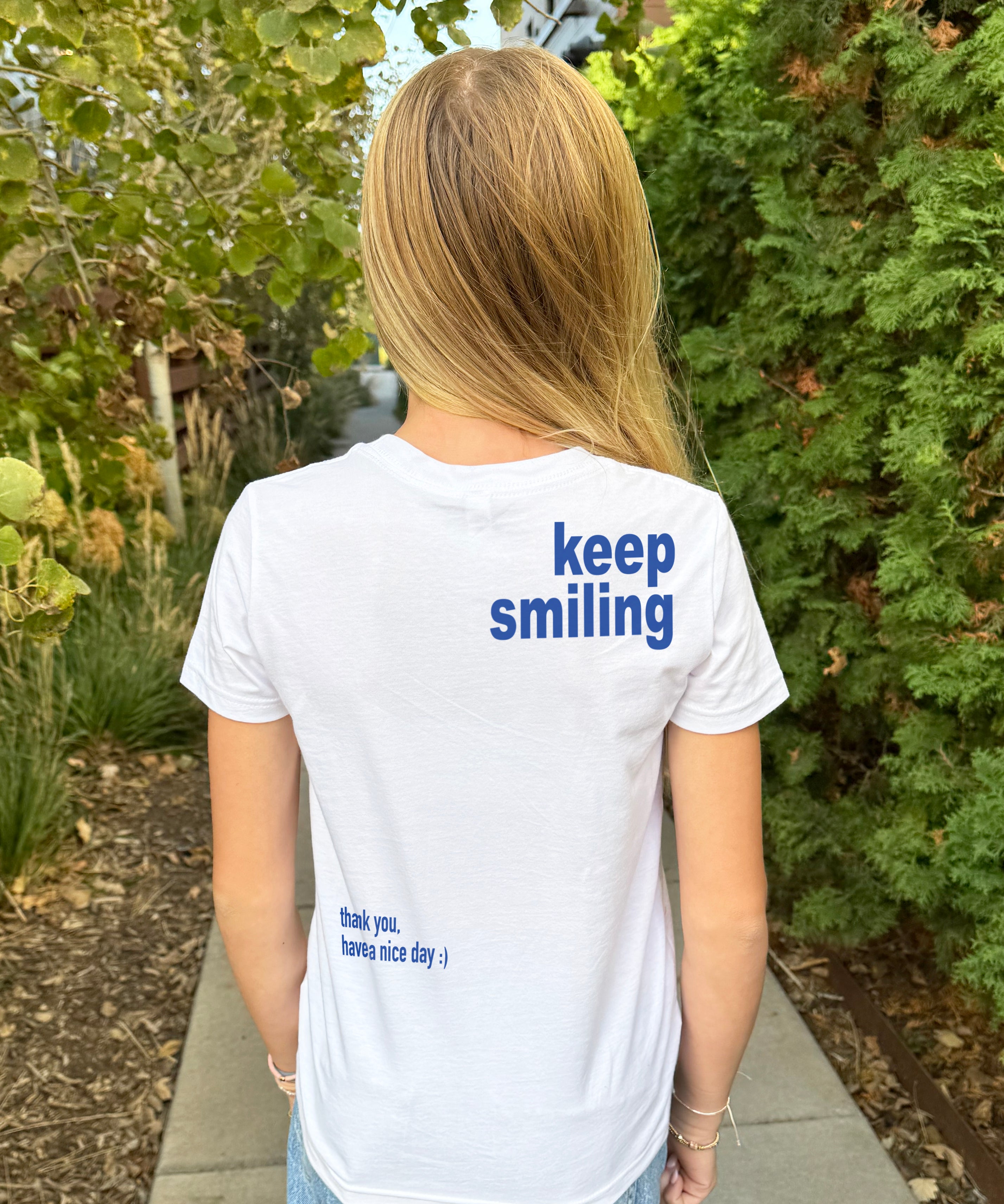 Girl in white tee shirt with bluelettering that say "Keep Smiling" from behind