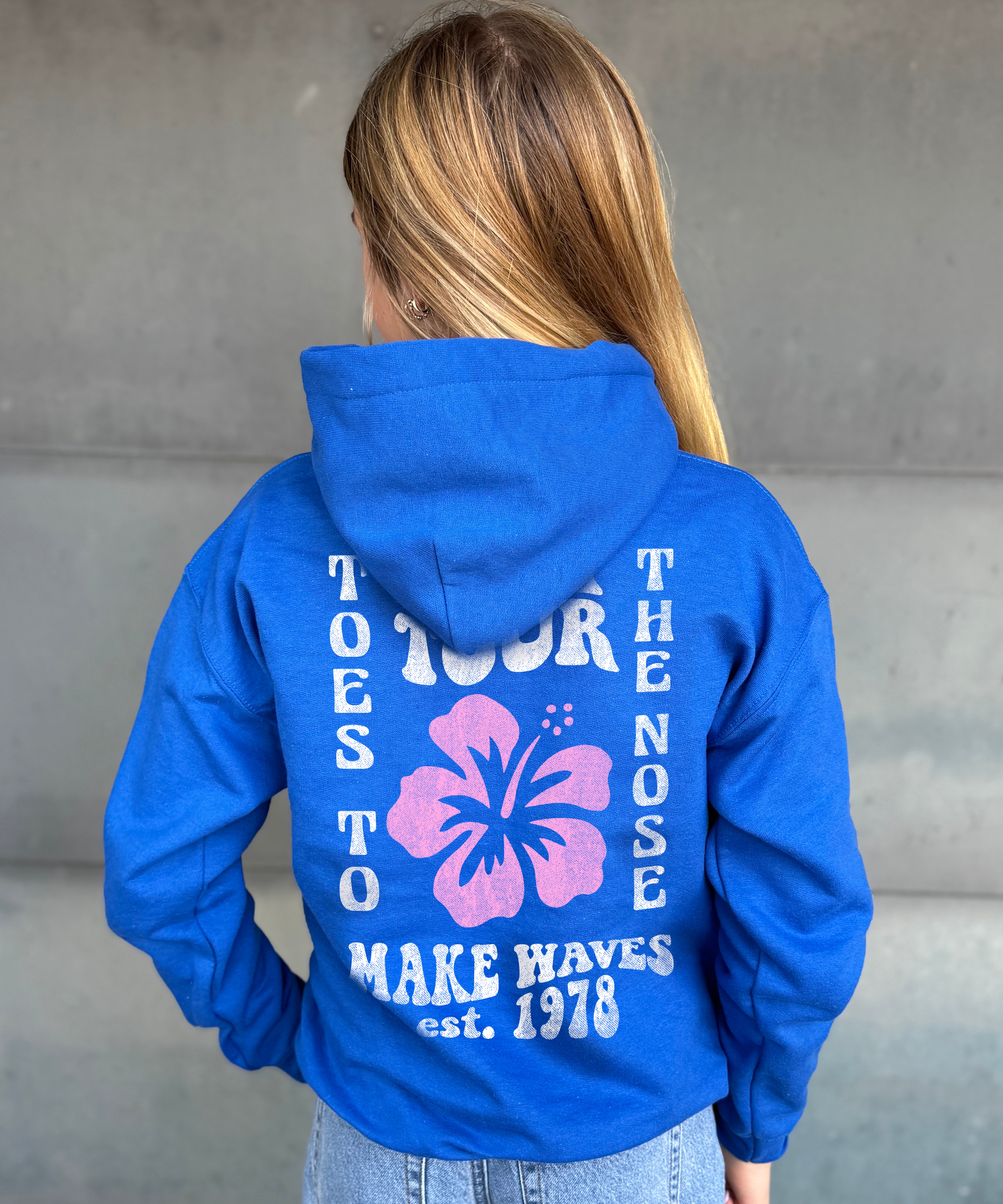 Girl in blue hoodie that says "Toes to the nose" in white text with Hawaiian flower