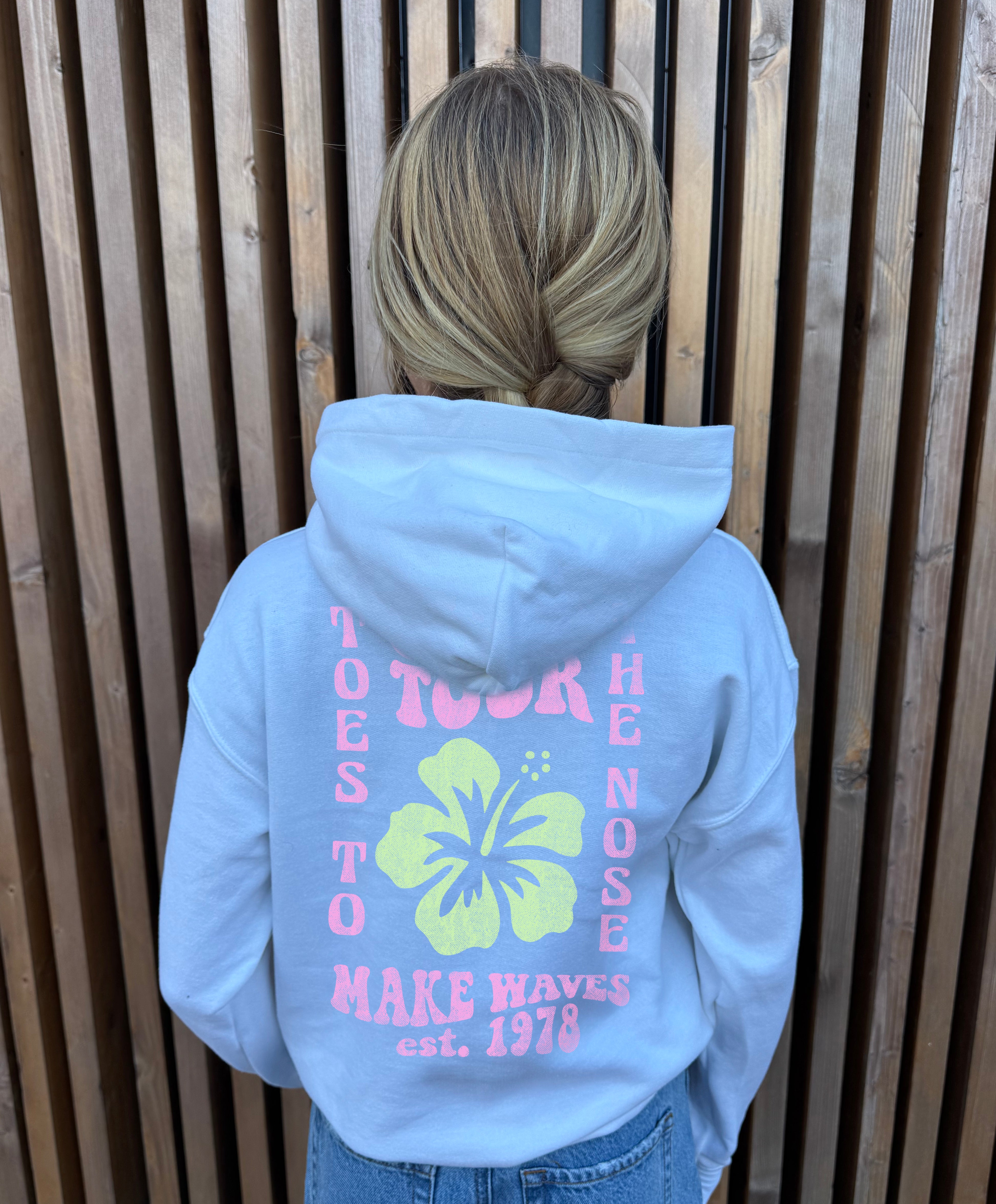 White hoodie from the back that says "toes to the nose" in pink text with a yellow Hawaiian flower