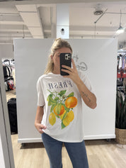 Woman in white tshirt that has black text that says "fresh" and a picture of oranges