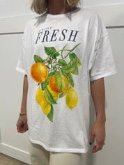 Woman in white tshirt that has black text that says "fresh" and a picture of oranges