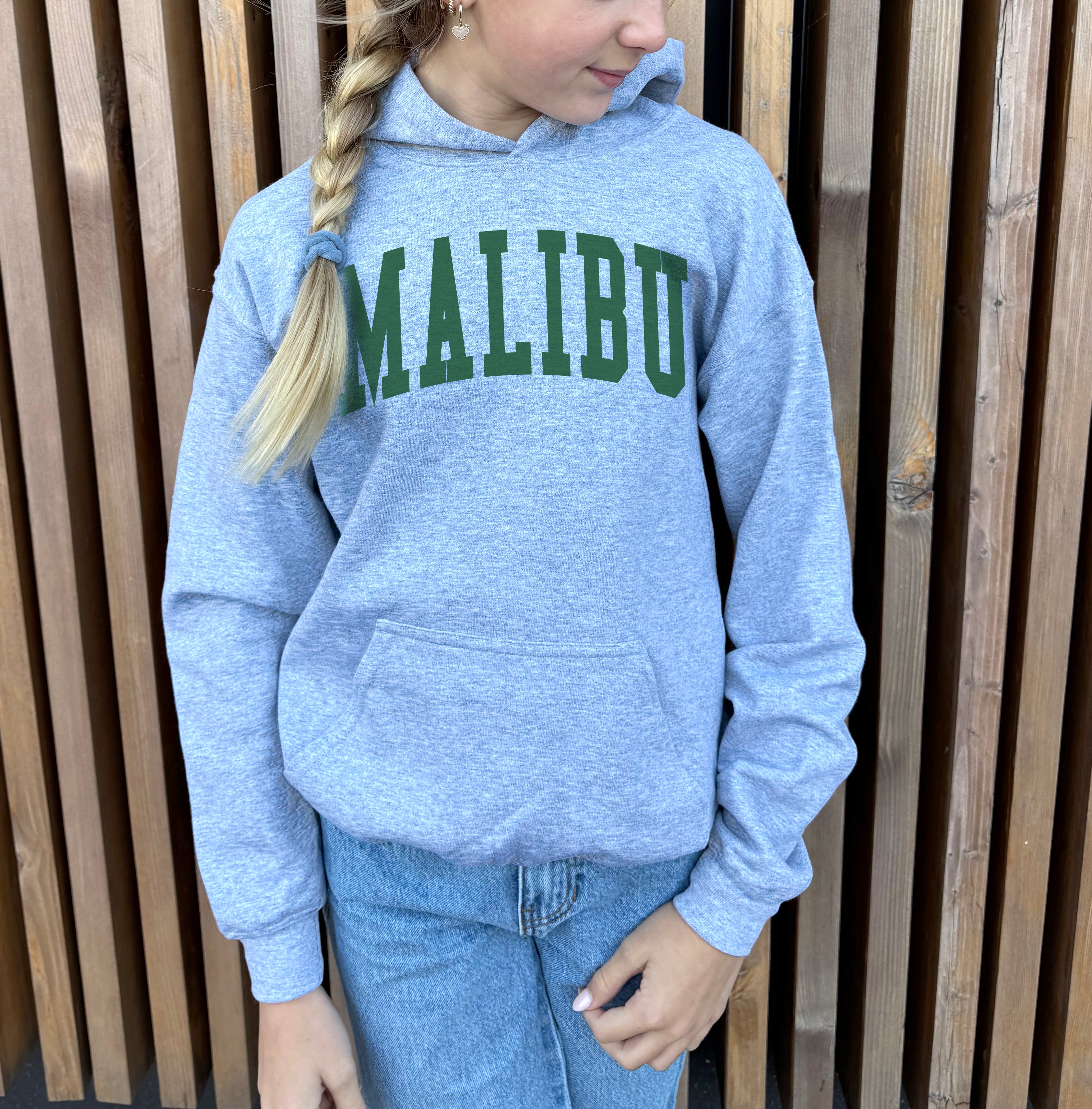 Girl in grey hoodie that says "Malibu" in green text