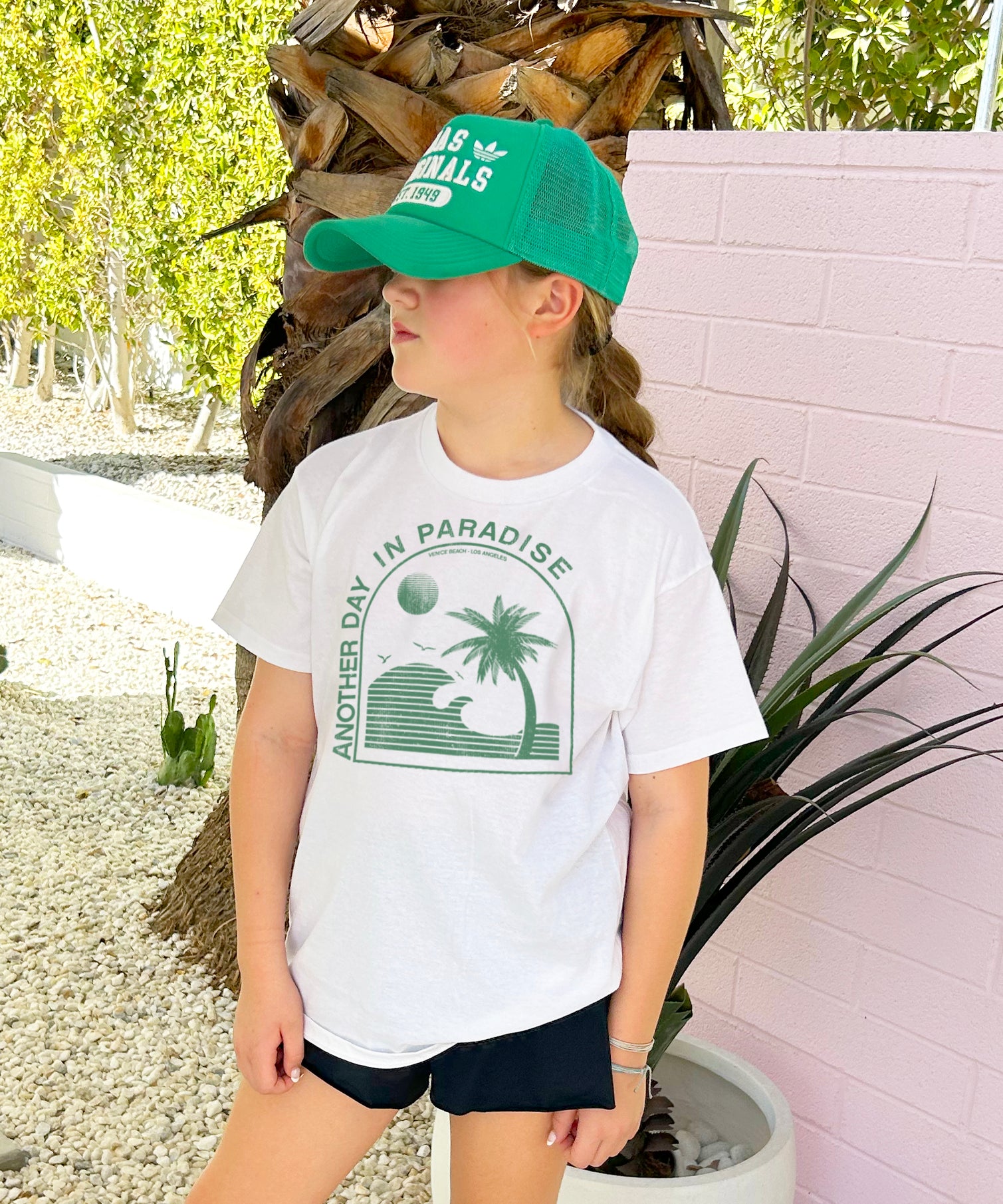 Girl in white shirt that says "Another Day in Paradise" in green text