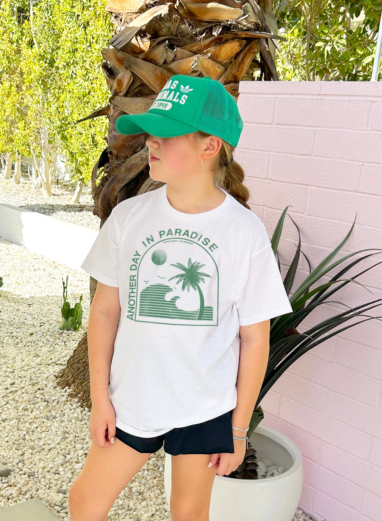 Girl in white shirt that says "Another Day in Paradise" in green text