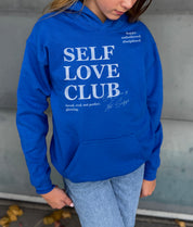 Girl in blue hoodie that says "Self Love Club" in white text 