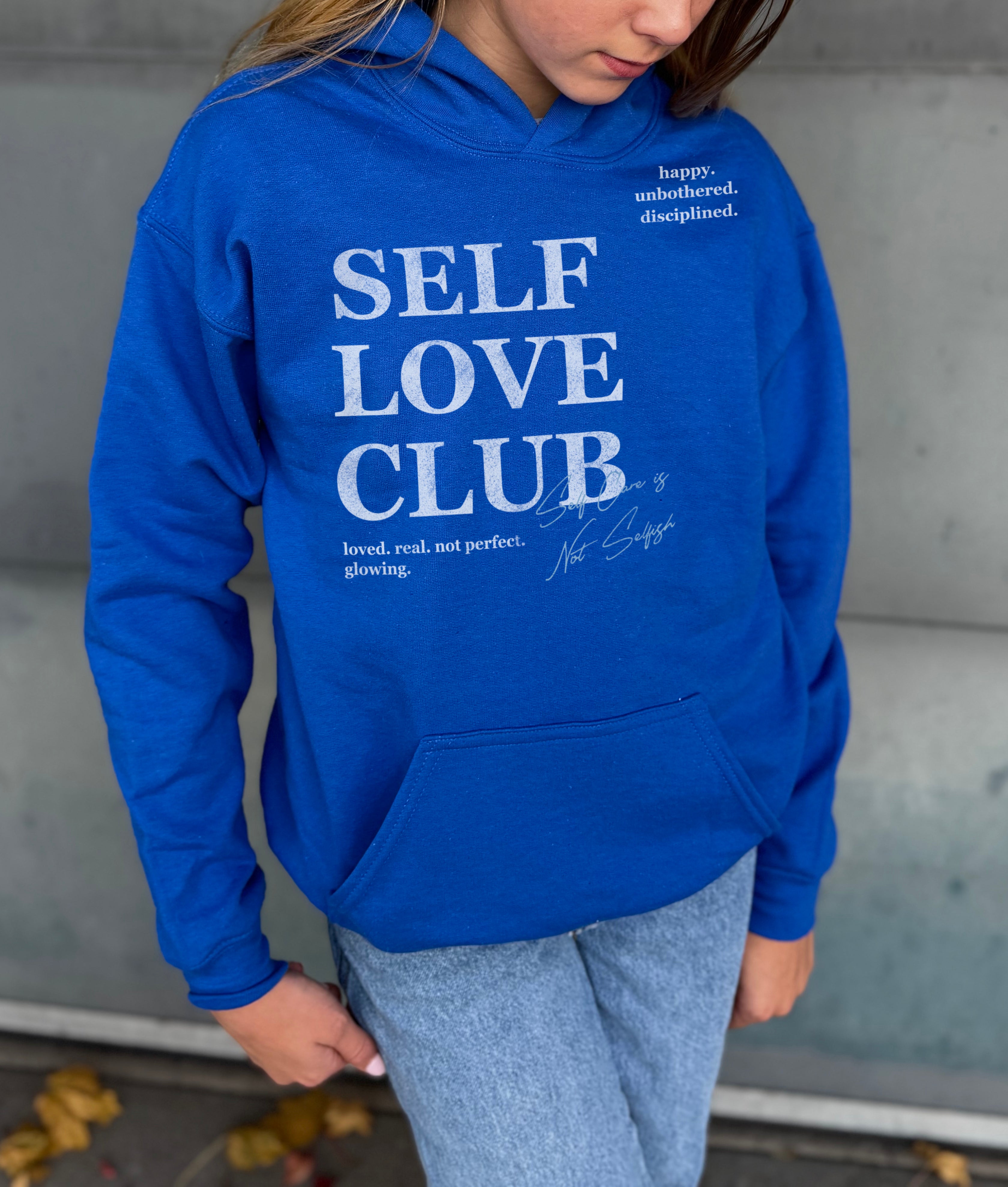 Girl in blue hoodie that says "Self Love Club" in white text 