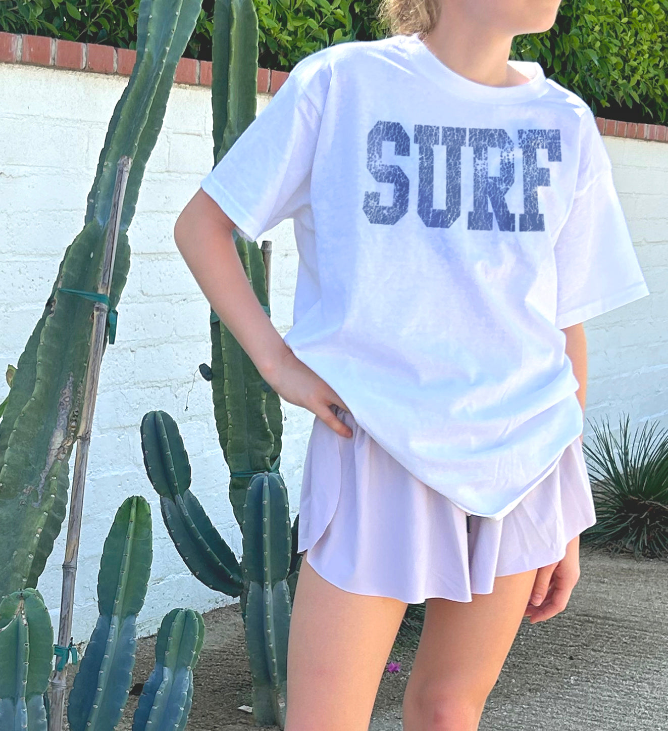 white tee shirt on girl that says "SURF" in blue lettering
